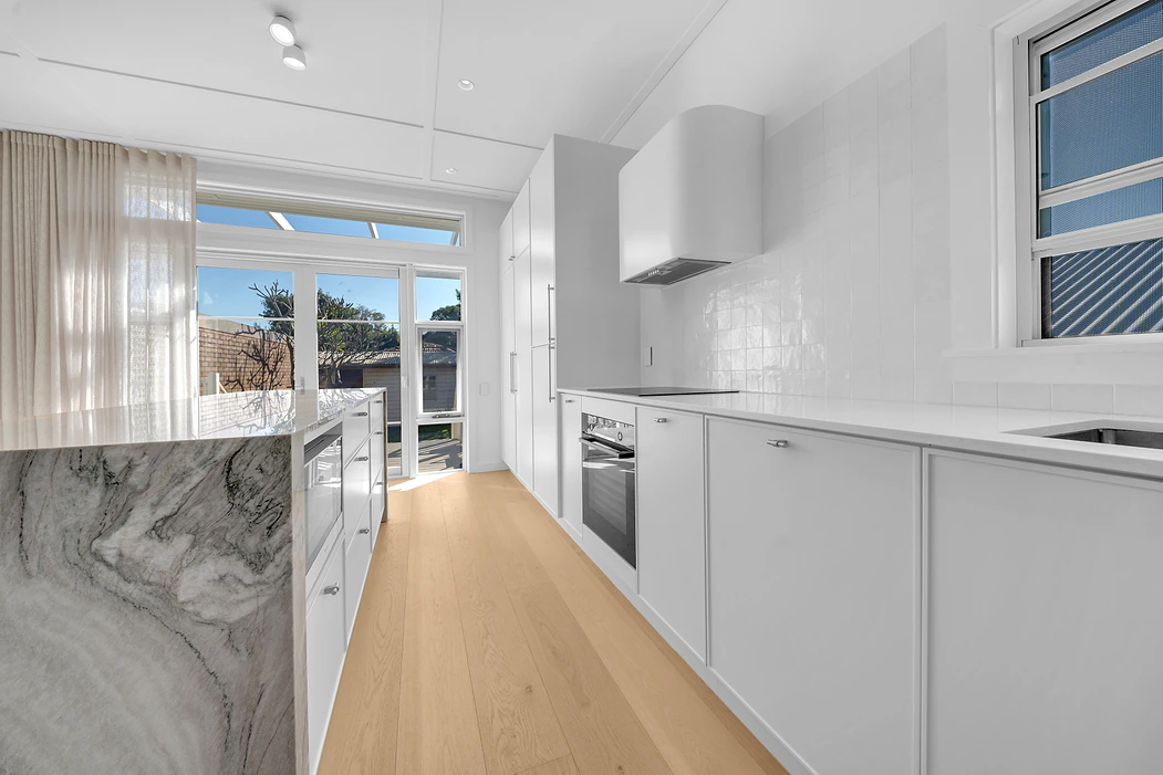 White galley kitchen with marble waterfall island and tiled splashback