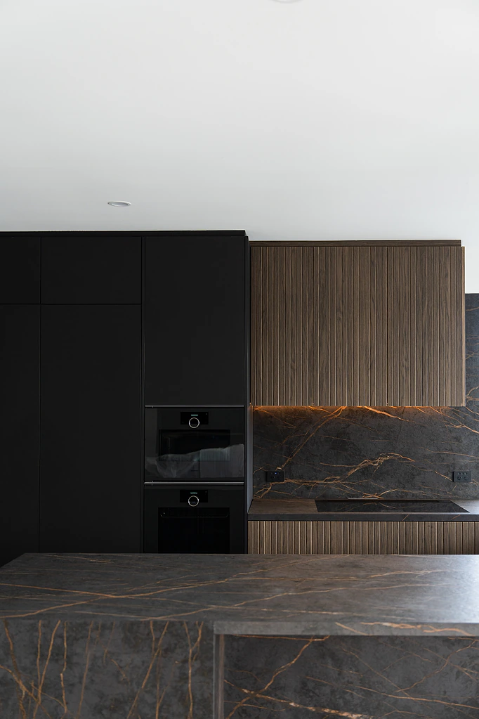 Dark kitchen with fluted timber rangehood and marble splashback