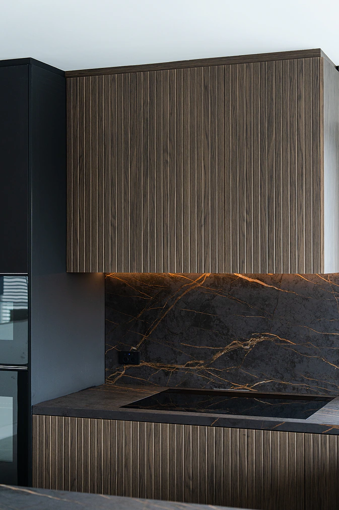 Fluted timber rangehood above a dark stone splashback with LED strip